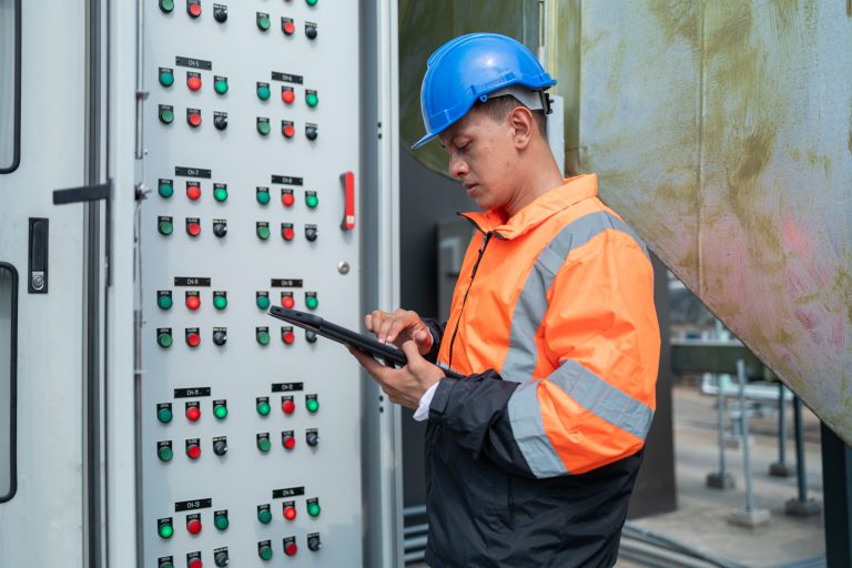 Building operations technician monitoring infrastructure systems through a control panel and tablet.