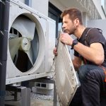 An HVAC technician performing preventive maintenance and cleaning on a residential outdoor air conditioning unit.