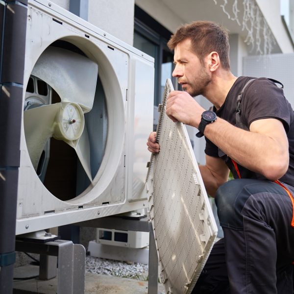 An HVAC technician performing preventive maintenance and cleaning on a residential outdoor air conditioning unit.