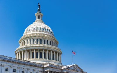 The white neoclassical dome of the United States Capitol Building with the American flag flying under a clear blue sky.