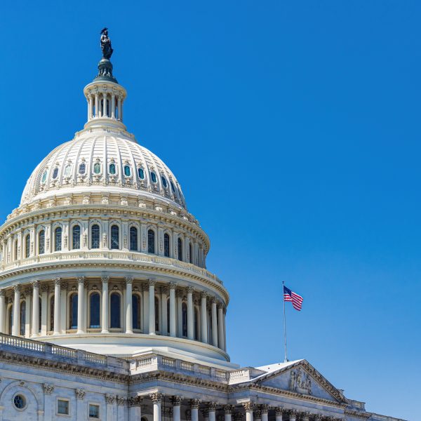 The white neoclassical dome of the United States Capitol Building with the American flag flying under a clear blue sky.