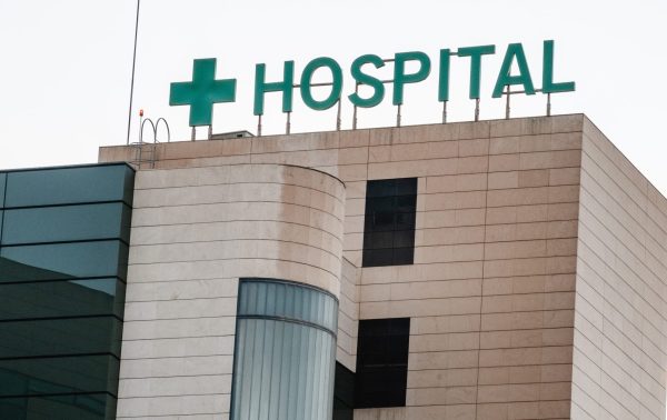 Exterior view of a modern hospital building with a green cross symbol and 'HOSPITAL' sign on the rooftop.