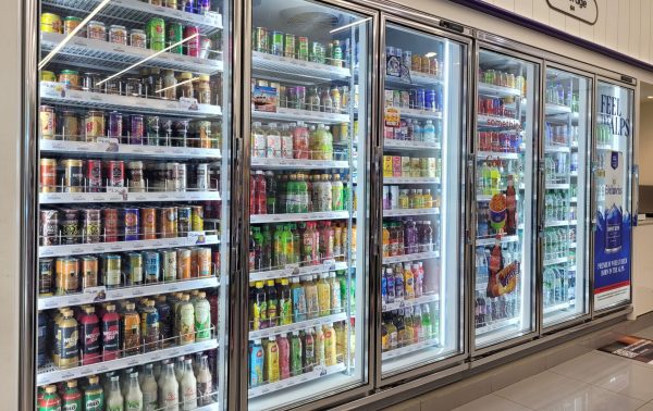 A row of glass-door commercial display freezers stocked with various canned and bottled beverages in a convenience store.